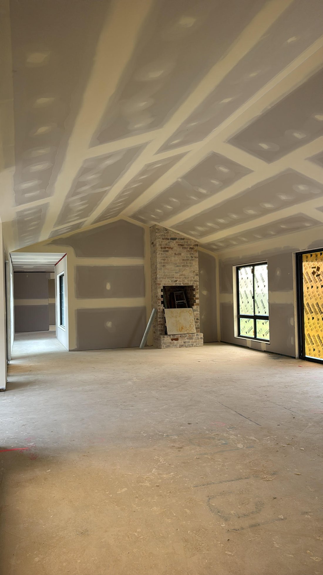 Open plan living with raked ceiling and brick fireplace during construction